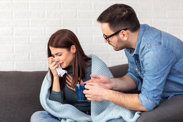 Couple sitting on sofa, ill woman with blanket over her body and man taking care