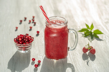 Fresh organic red smoothie in glass mug on white table, close up. Refreshing summer fruit drink. The concept of healthy eating. Cranberry and raspberry smoothie