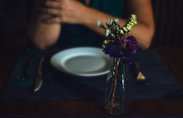 Romantic dinner with a caucasian woman. Selective focus on the dried flowers in the center of the table.  Blurred background.