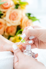 Pedicurist applying white color to foot nails of woman