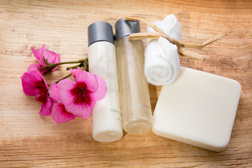 two miniature hotel conditioner and shampoo bottles and a bar of soap on a wooden tray background with a pink flower