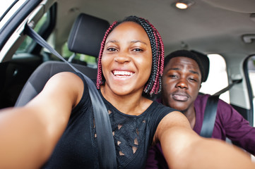 Beautiful young african american couple sitting on the front passenger seats while handsome man driving a car. Making selfie together.