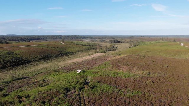 An aerial sideway right to left footage of the New Forest with trees, heartland and trail path under a majestic blue sky and some white clouds