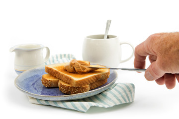 table setting of peanut butter on toast on a blue plate with a coffee cup and creamer isolated on white