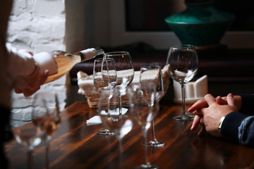 Fototapeta na wymiar Wine glasses on a table in a restaurant. Wine tasting. Male hands and the hands of a waiter. Wine is pouring into a glass. Out of focus. Photo without a face.