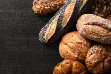 Mixed baguettes and bread rolls on dark grey wood. Top view. Space for text.