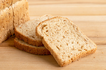 Three slices of whole wheat toast bread isolated on light wood next to a loaf of bread.