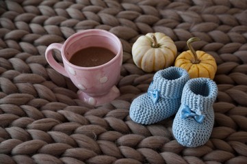 knitted baby shoes on merino wool scarf with cup of coffee and pumpkins. autumn baby clothes.