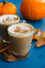 Pumpkin spiced coffee with milk and cinnamon in a glass mug. Autumn or winter hot drink on a blue wooden table. Close up