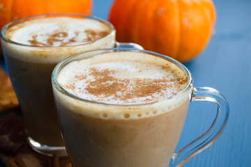 Pumpkin spiced coffee with milk and cinnamon in a glass mug. Autumn or winter hot drink on a blue wooden table. Close up