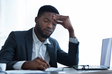 Serious afro businessman filling paperwork at workplace in modern office