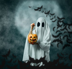 White ghost holding a carved pumpkin with candies in Halloween night.