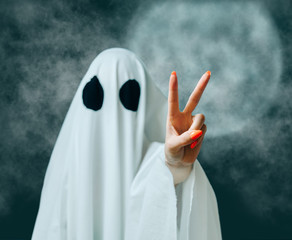 White ghost showing peace gesture in Halloween full moon night.