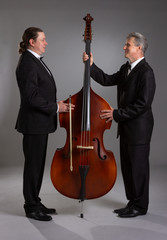 Portrait of two men men with double bass on a gray background.