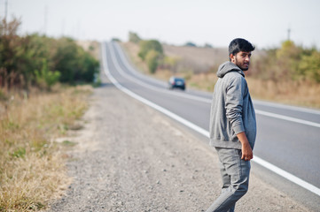 Hitchhiking indian man travelling by hitchhike on road side on highway.