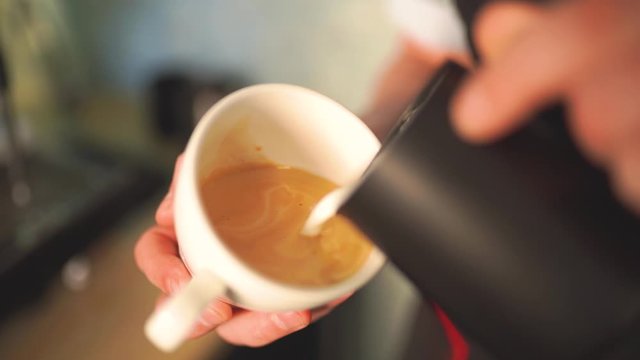 Slow motion of barista pouring milk over coffee creating a perfect cappuccino or latte