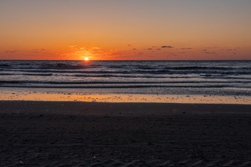 Beautiful sunset landscape at the North sea and orange sky above it with awesome sun golden reflection on waves as a background. Amazing summer sunset view on the beach.