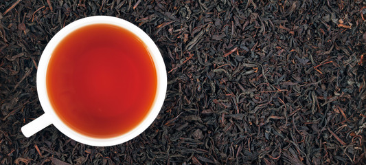 Cup of tea on the dry leaves of black tea. Panorama. Banner.