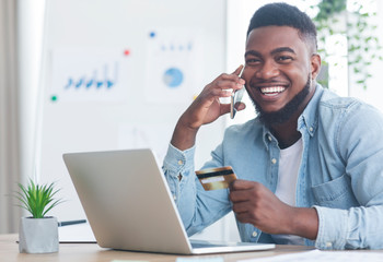 Cheerful black guy talking on phone and holding credit card