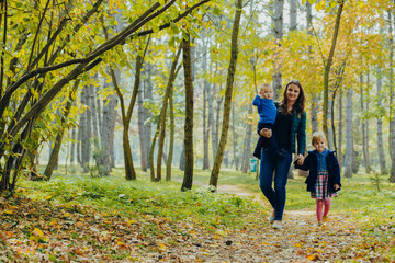 Fototapeta premium Mom with daughter and son are walking in the autumn park. Family for a walk in the forest