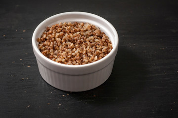 Cooked buckwheat porridge in a deep plate on a black wooden background. Copy space.