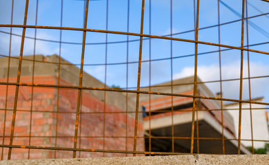 Obraz premium View through the metal grid on unfinished house. Building under construction against a backdrop of mountains and blue sky. Construction of residential building in Europe. European building technology.