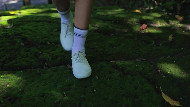 Close up of young woman feet walking by the road overgrown with tropical moss. Happy tourist girl on vacation. Lifestyle backpack tourist travel alone on holiday. An independent female researcher.