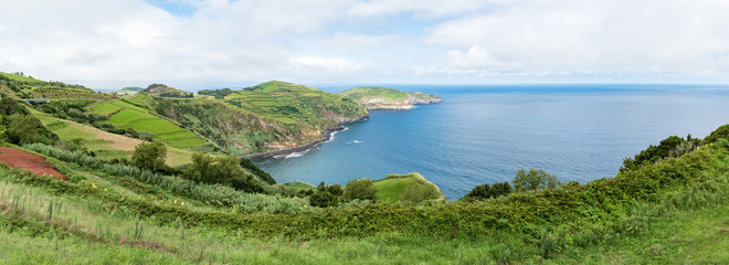 Panoramic view from the Miradouro de Santa Iria on the island of São Miguel in the Azores. The view shows part of the northern coastline with beaches, cliffs and lush green fields on the clifftop.