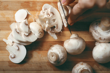 Woman cutting mushrooms on wooden plank, close up