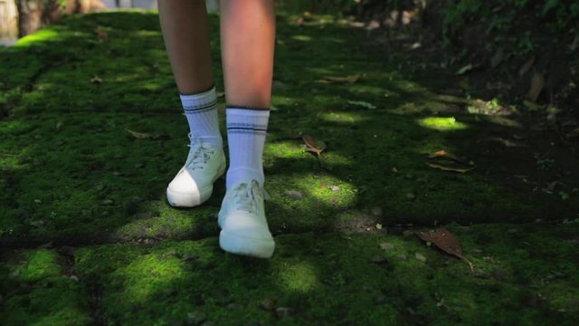 Close up of young woman feet walking by the road overgrown with tropical moss. Happy tourist girl on vacation. Lifestyle backpack tourist travel alone on holiday. An independent female researcher.