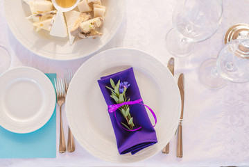 Served plate with Cutlery and a bright purple napkin with a sprig of eucalyptus in the decor of a wedding dinner or holiday