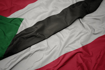 waving colorful flag of poland and national flag of sudan.