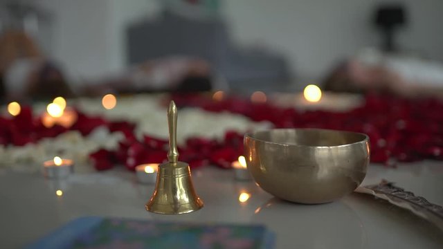 Close up shot of tibetian singing bowl, handbell, tarot cards against the background of rose petals and candles burning during a spiritual female practice.