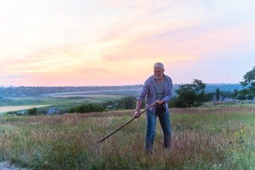 Old man with grey hair and beard mowing grass in a field