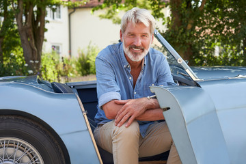 Portrait Of Proud Mature Man Sitting In Restored Classic Sports Car Outdoors At Home