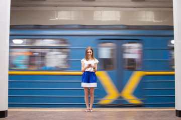 girl stands on a subway platform and listens to music on the background of a passing train, a student uses a phone in the subway, copy space