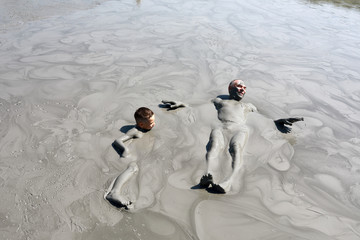 Grandfather and grandson lying in mud pool