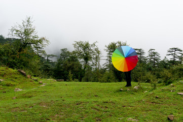 Young indian girl with face hidden holding a colorful umbrella in a foggy feild with fog