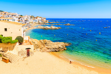 Young woman sitting on sandy beach in picturesque fishing village of Calella de Palafrugell, Catalonia, Spain