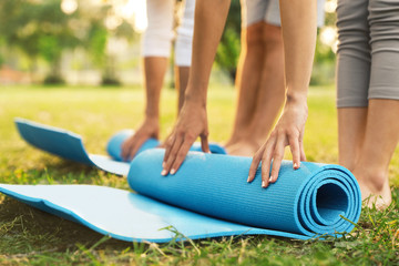 People rolling up yoga mat in park at morning, closeup - Powered by Adobe