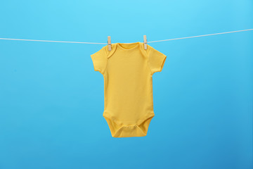 Baby onesie hanging on clothes line against blue background. Laundry day