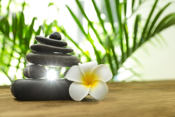 Table with stack of stones, flower and blurred green leaves on background, space for text. Zen concept