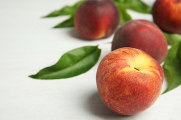 Fresh peaches and leaves on white table, space for text