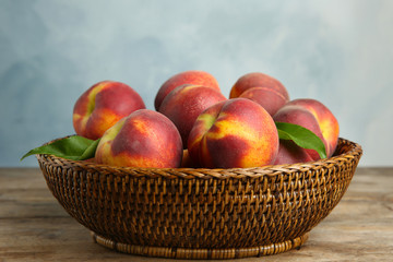 Wicker bowl with tasty peaches on wooden table against blue background