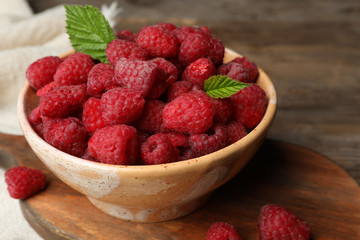 Bowl with delicious ripe raspberries on cutting board, closeup