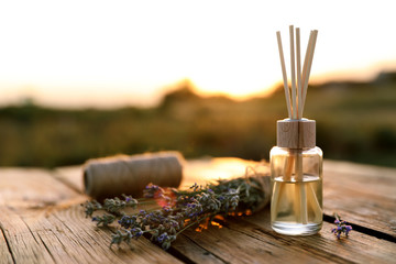 Reed air freshener and fresh lavender flowers on wooden table in field. Space for text