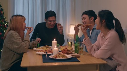 Merry Christmas and Happy New Year! Young friends group having dinner at home. Asian family party with beer and pizza food near christmas tree at house in night. Celebration holiday and togetherness.