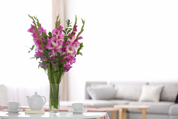 Vase with beautiful pink gladiolus flowers on wooden table in living room. Space for text