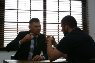 Angry detective interviewing criminal in interrogation room - obrazy, fototapety, plakaty