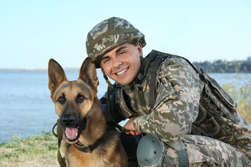 Man in military uniform with German shepherd dog near river